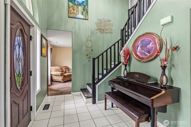 tiled entrance foyer with a high ceiling, visible vents, stairway, and baseboards