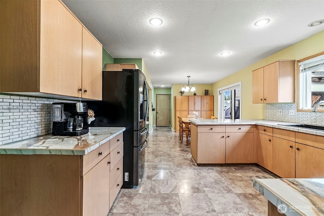 kitchen with a peninsula, a sink, light countertops, black fridge, and decorative backsplash