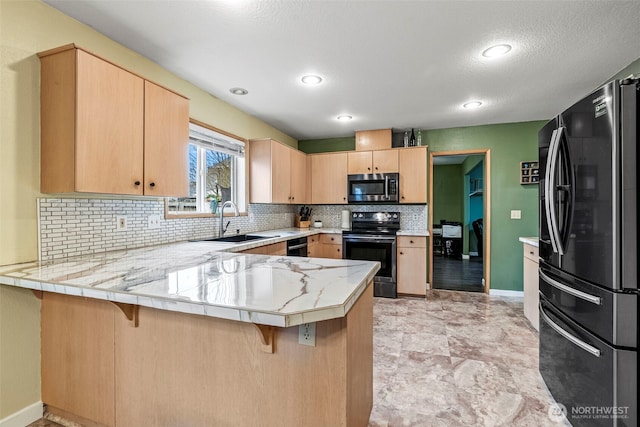 kitchen with a peninsula, light countertops, light brown cabinetry, black appliances, and a sink