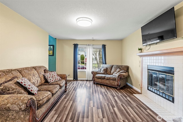 living room with a textured ceiling, baseboards, wood finished floors, and a tile fireplace