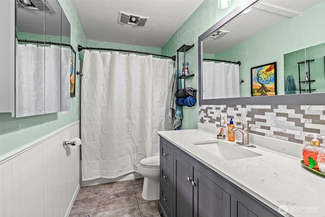 full bathroom with a wainscoted wall, visible vents, decorative backsplash, toilet, and vanity