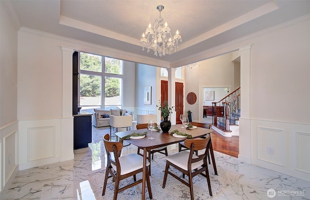 dining space featuring marble finish floor, stairway, a raised ceiling, and a decorative wall