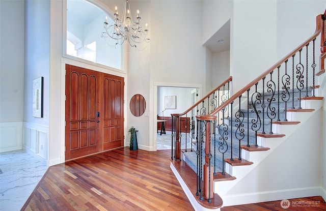 entryway with a wainscoted wall, a high ceiling, wood finished floors, a chandelier, and stairs