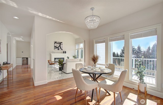 dining area featuring a glass covered fireplace, wine cooler, wood finished floors, an inviting chandelier, and recessed lighting