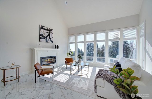 living area with marble finish floor, plenty of natural light, baseboards, and a glass covered fireplace