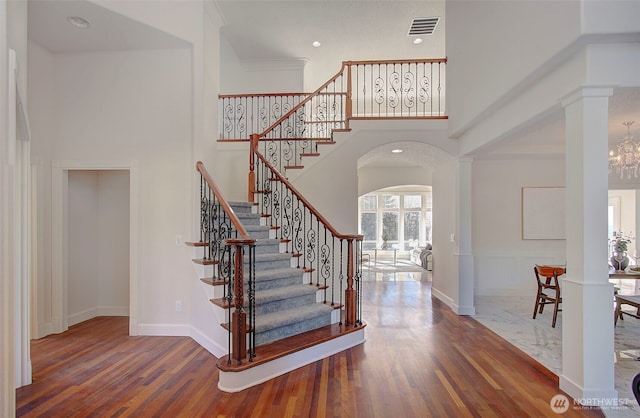 staircase featuring visible vents, a towering ceiling, ornate columns, and wood finished floors