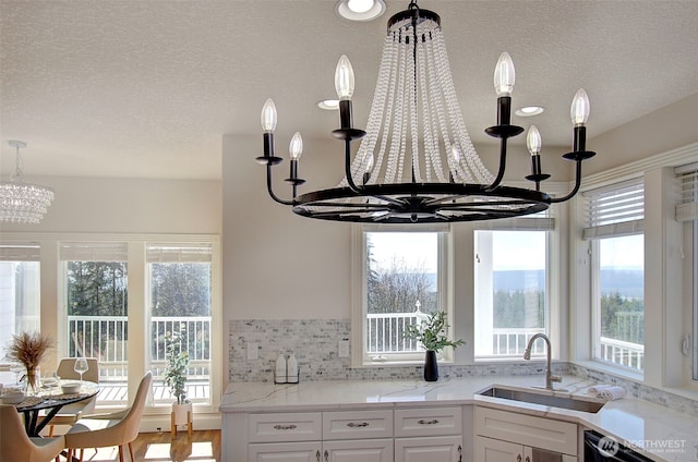 kitchen featuring white cabinets, dishwasher, an inviting chandelier, light countertops, and a sink