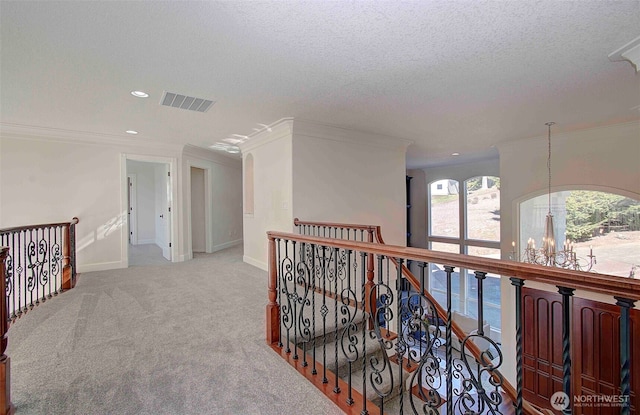 hall featuring visible vents, carpet flooring, a textured ceiling, an upstairs landing, and a chandelier