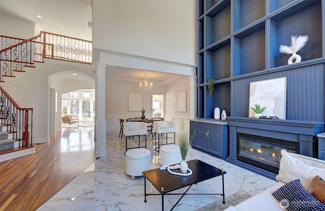 living area featuring arched walkways, stairs, marble finish floor, wainscoting, and a glass covered fireplace