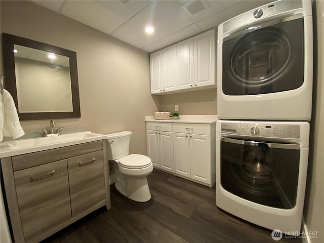 washroom with stacked washer and dryer, dark wood-style floors, laundry area, and a sink