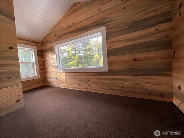 spare room featuring vaulted ceiling, wood walls, and carpet