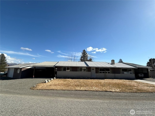 single story home with a carport, a chimney, metal roof, and gravel driveway