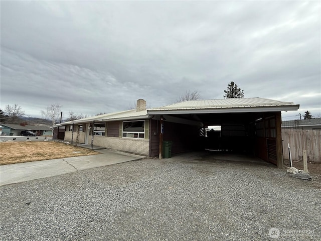 exterior space with brick siding, a chimney, metal roof, a carport, and driveway