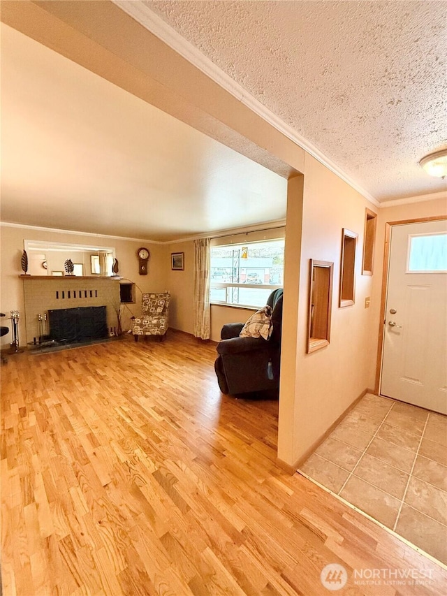 unfurnished living room with a fireplace with raised hearth, ornamental molding, plenty of natural light, a textured ceiling, and light wood finished floors