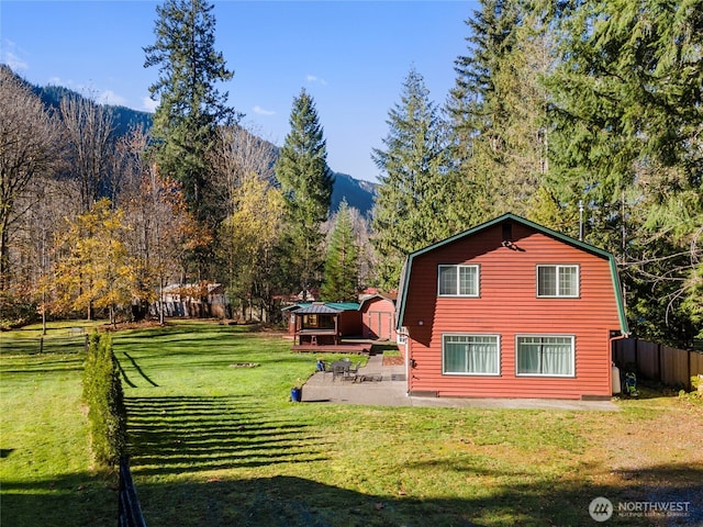 back of house with a patio, a lawn, a gambrel roof, fence, and a forest view