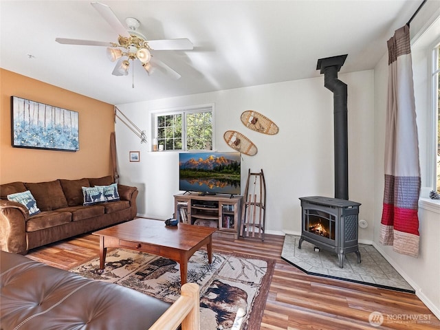 living area with a wood stove, ceiling fan, baseboards, and wood finished floors