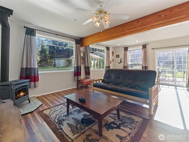 living room with a wood stove, ceiling fan, wood finished floors, beamed ceiling, and baseboards