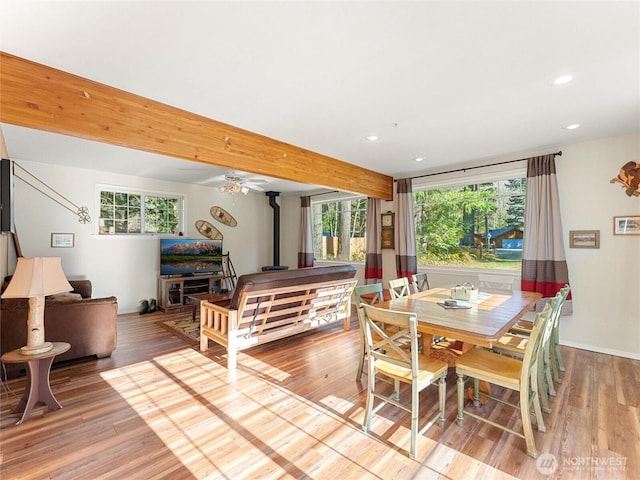 dining room featuring a wood stove, beam ceiling, and wood finished floors