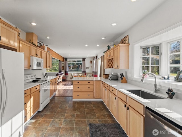 kitchen featuring a peninsula, white appliances, a sink, and light brown cabinetry