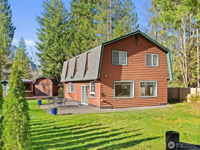 back of house featuring a gambrel roof, an outbuilding, fence, a patio area, and a shed