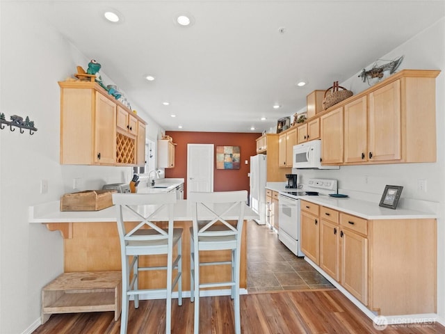 kitchen featuring light brown cabinets, a peninsula, white appliances, a sink, and a kitchen breakfast bar