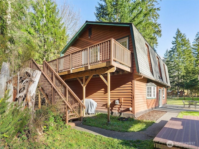 back of house featuring a deck, a shingled roof, stairway, and a gambrel roof