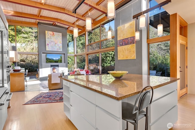 kitchen with light wood finished floors, a wall of windows, light stone counters, and white cabinets