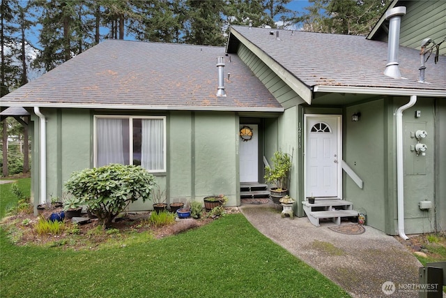 view of front of home featuring entry steps, stucco siding, a shingled roof, and a front yard