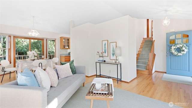 living area featuring stairs, vaulted ceiling, a notable chandelier, and light wood finished floors