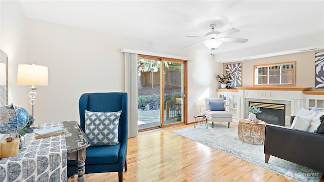 living area with a glass covered fireplace, a ceiling fan, and hardwood / wood-style flooring