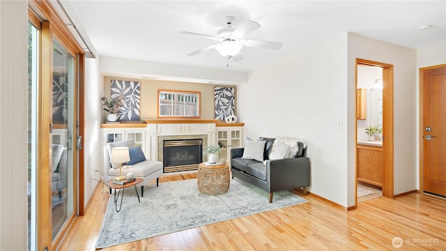 living room featuring a ceiling fan, plenty of natural light, a fireplace, and light wood-type flooring