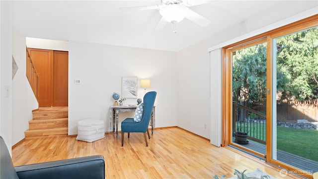 sitting room with ceiling fan, baseboards, light wood-style flooring, and stairs