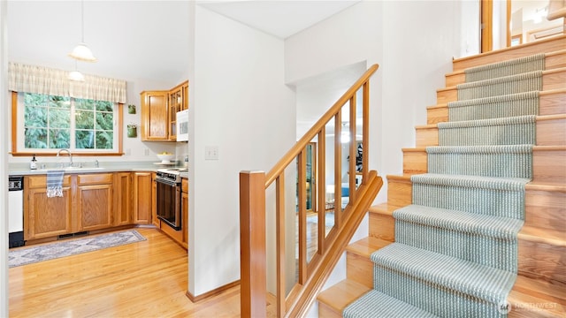 kitchen featuring white appliances, light wood finished floors, a sink, light countertops, and decorative light fixtures