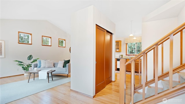 corridor with light wood-style floors, stairs, and vaulted ceiling