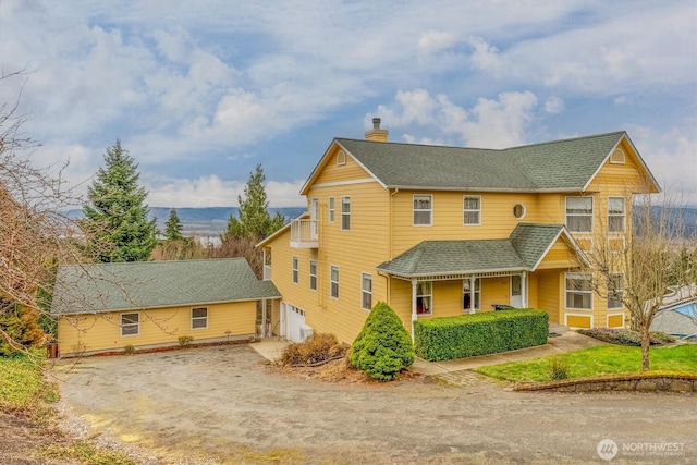 view of front of home featuring dirt driveway, roof with shingles, a chimney, and a garage