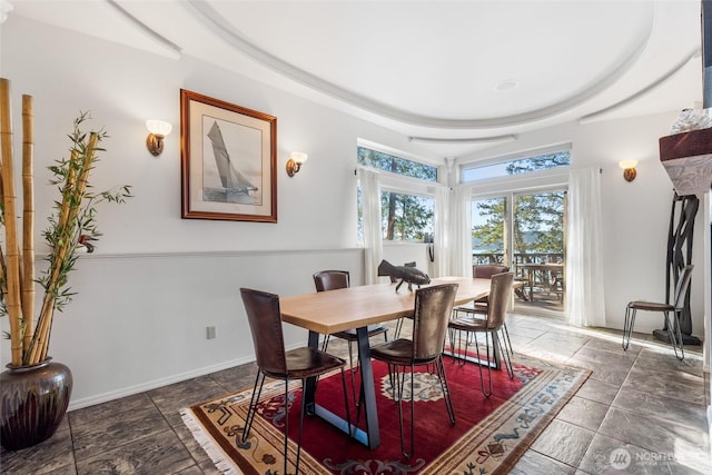 dining room featuring stone finish floor, baseboards, and a tray ceiling