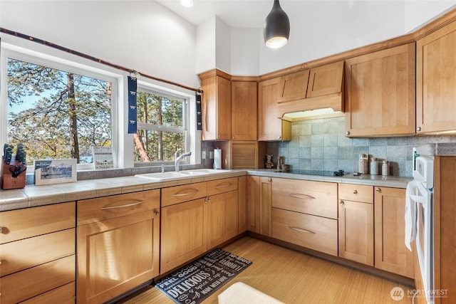 kitchen with tile countertops, oven, a sink, light wood finished floors, and tasteful backsplash