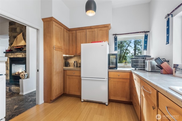 kitchen with a fireplace, tile countertops, light wood-style floors, freestanding refrigerator, and brown cabinetry