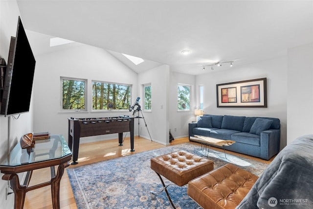 living area featuring lofted ceiling with skylight, light wood-style flooring, and baseboards