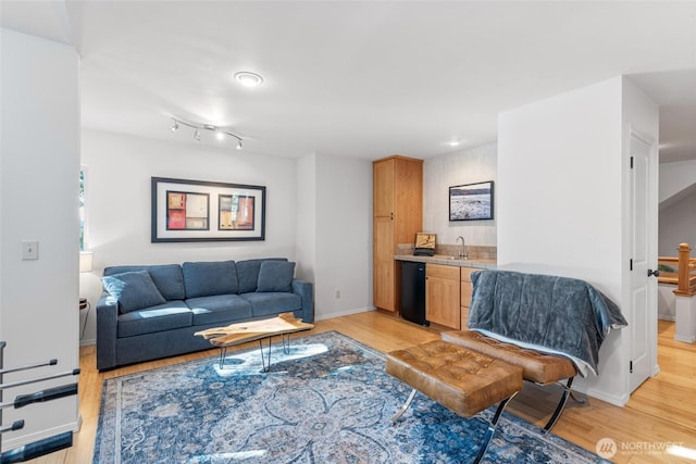 living room featuring light wood-style floors, indoor wet bar, and baseboards