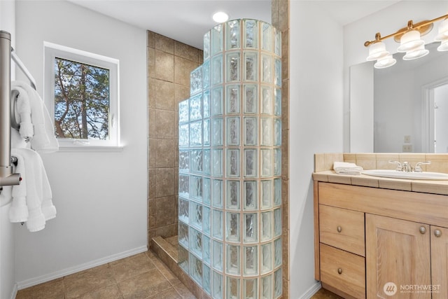 bathroom featuring tile patterned flooring, vanity, baseboards, and a walk in shower