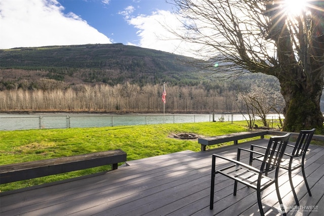 wooden terrace featuring an outdoor fire pit, fence, a yard, and a water view