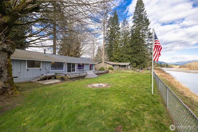 view of yard featuring fence, a fire pit, and a deck with water view