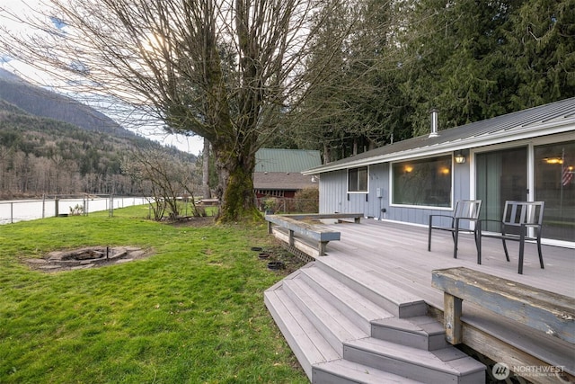 wooden deck with a forest view, a fire pit, a yard, and fence