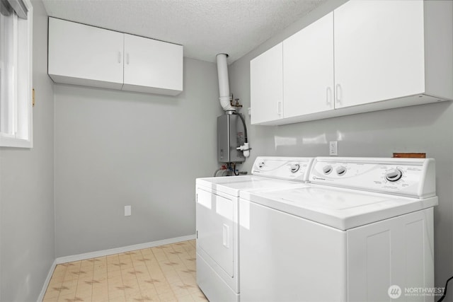 clothes washing area with independent washer and dryer, a textured ceiling, cabinet space, tankless water heater, and light floors