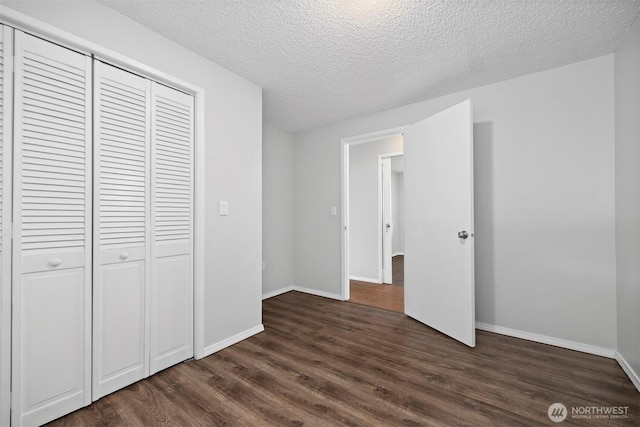 unfurnished bedroom featuring dark wood-style floors, a textured ceiling, baseboards, and a closet