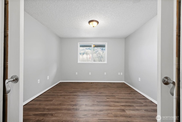 empty room featuring dark wood-type flooring, baseboards, and a textured ceiling