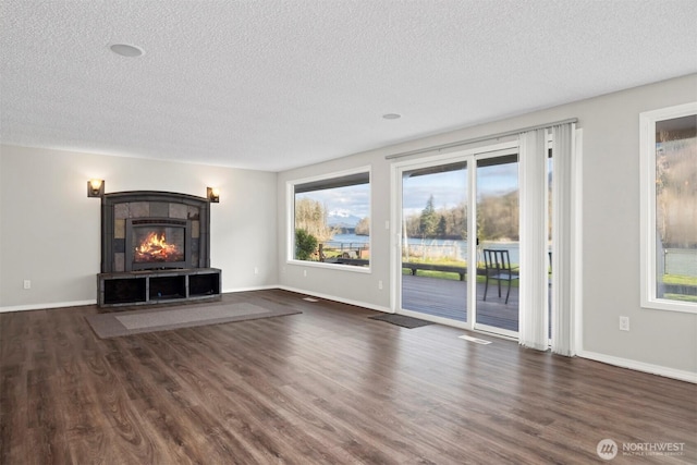 unfurnished living room featuring a tiled fireplace, baseboards, and wood finished floors