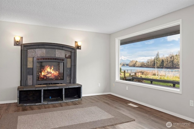 unfurnished living room featuring baseboards, a textured ceiling, wood finished floors, and a tiled fireplace