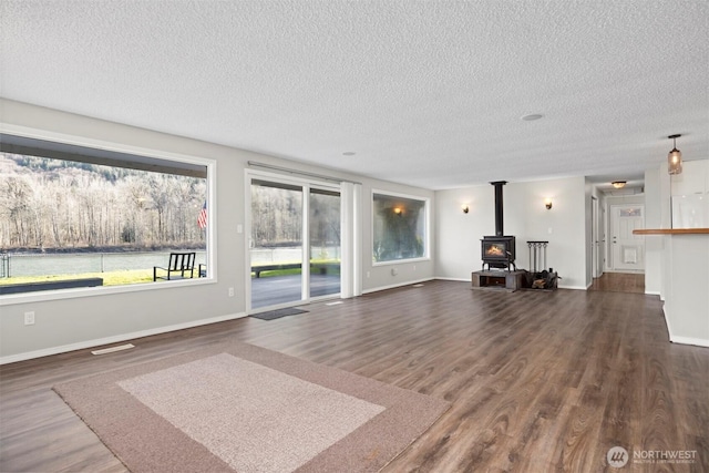 unfurnished living room featuring a textured ceiling, a wood stove, baseboards, and dark wood-style flooring